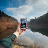 An hand holding a phone in front of a lake